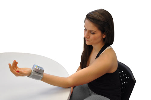 Woman seated at white table wearing a digital wrist device on her extended left arm monitoring health data