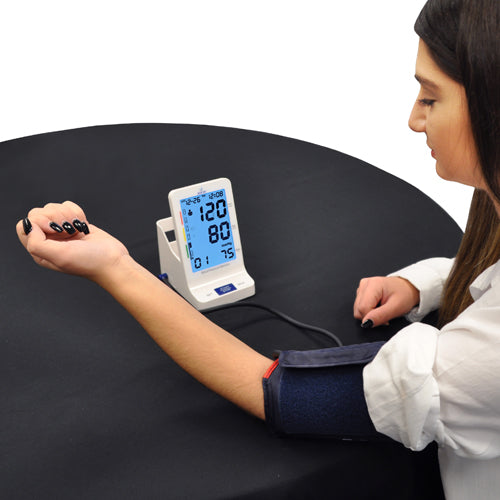 Woman with rolled-up sleeve measuring blood pressure using digital monitor on black table surface