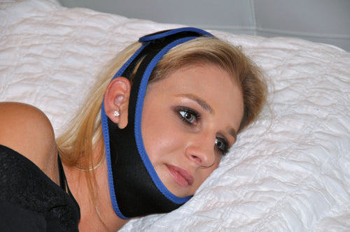 Woman lying on white pillow wearing black and blue chin strap for jaw support